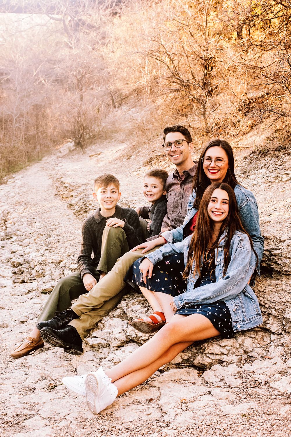 A family of four sits together on a rocky path during a golden autumn afternoon in nature.