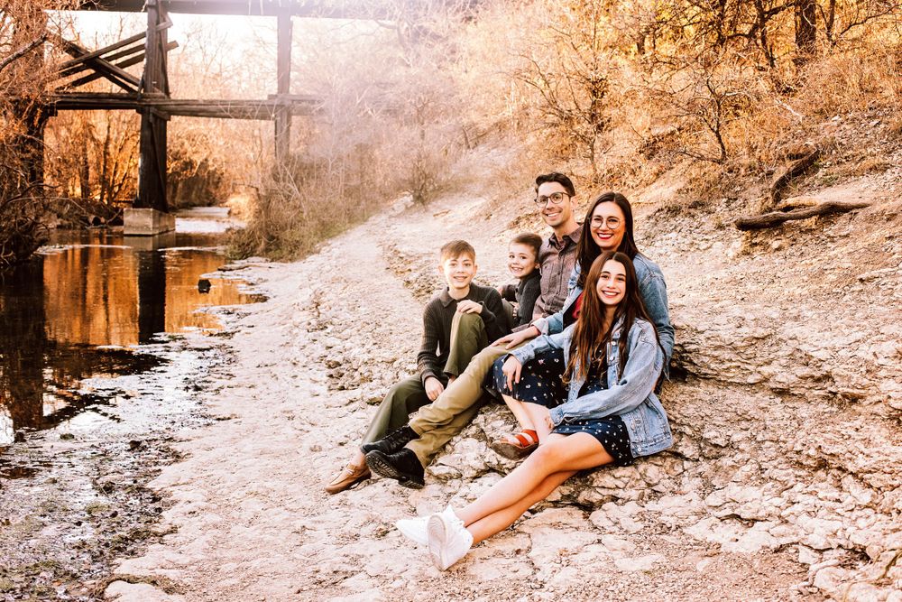 A group sits together on a rustic dirt path near a wooden bridge during autumn.