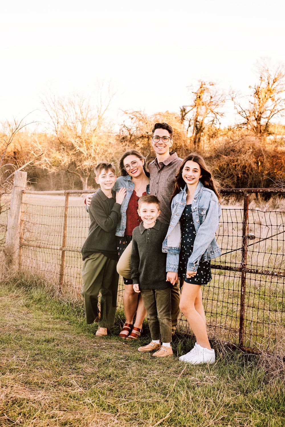 Group poses together along a rustic fence at golden hour in a countryside setting during autumn.