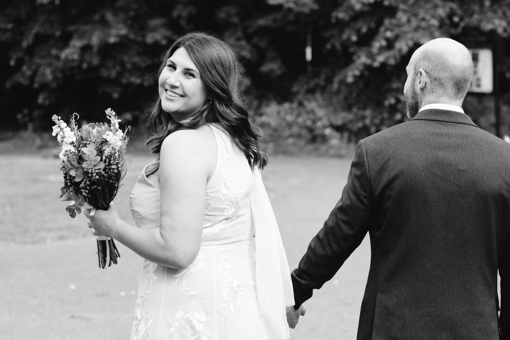 Black and white portrait of wedding couple holding hands outdoors at garden venue.