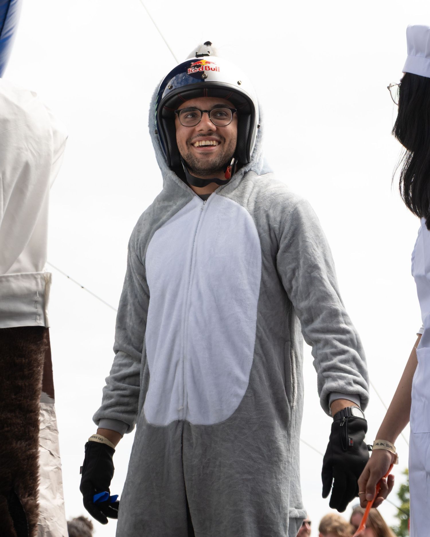 Person wearing a gray animal onesie costume smiles at an outdoor event.