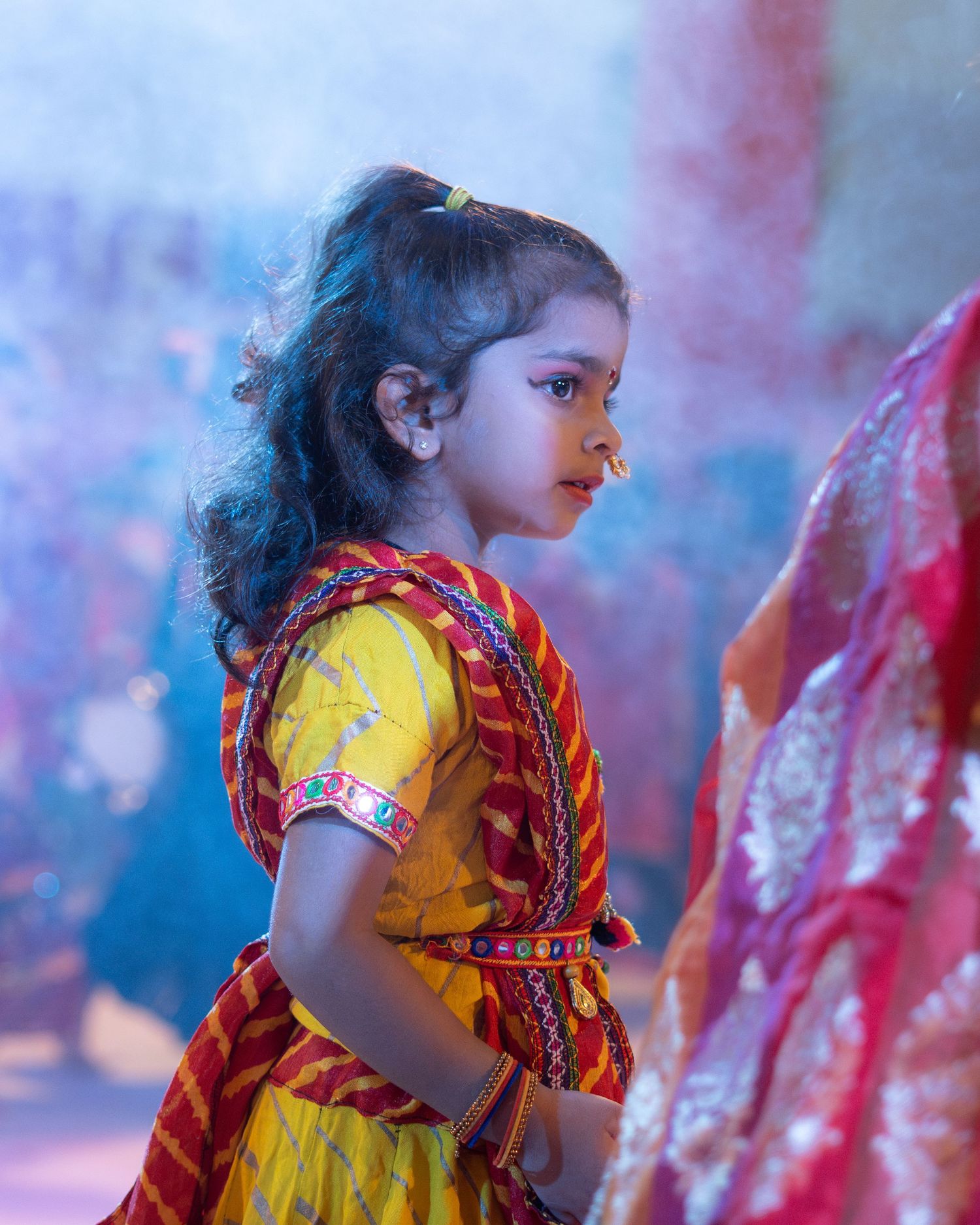 Young child in traditional yellow and red Indian dress celebrates during a colorful festival.