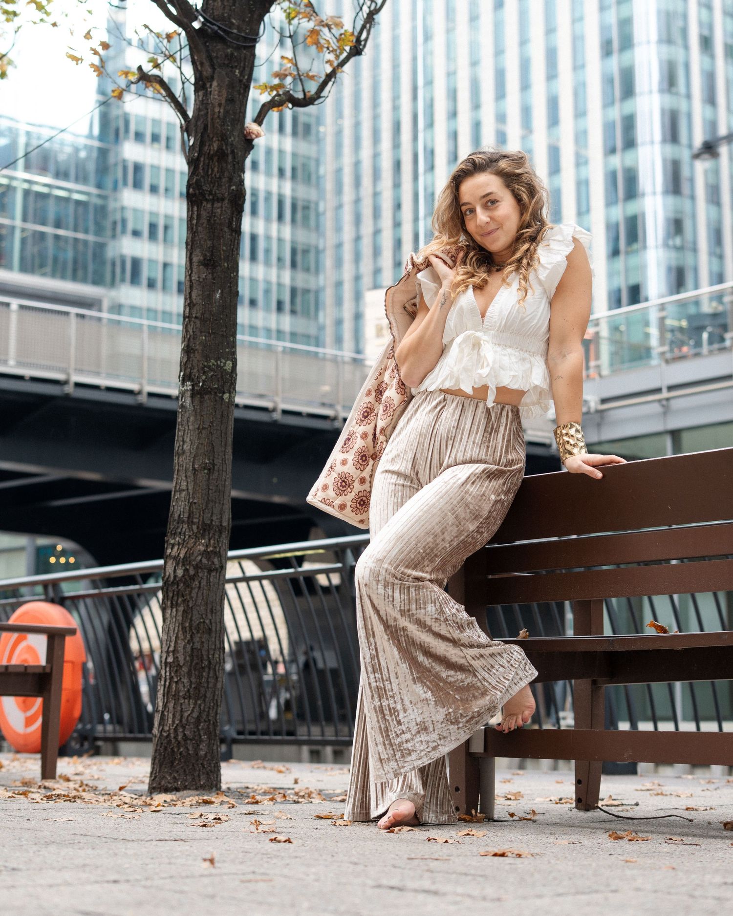 Fashionable outfit featuring velvet wide-leg pants and white top against urban backdrop with modern buildings.