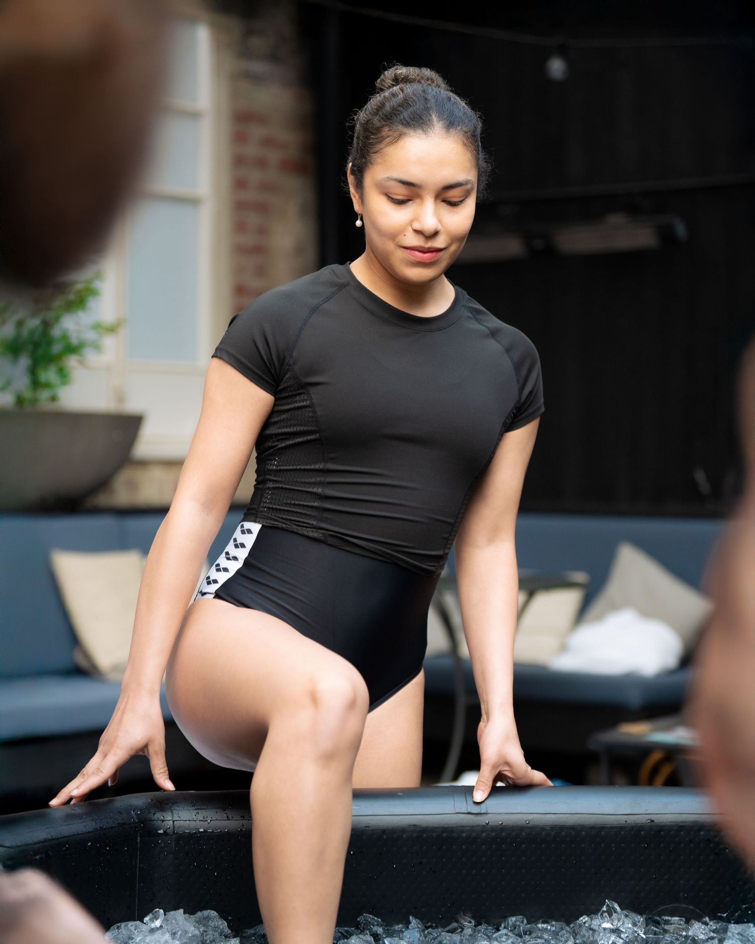 Athletic woman in black swimwear getting into hot tub during outdoor spa session.