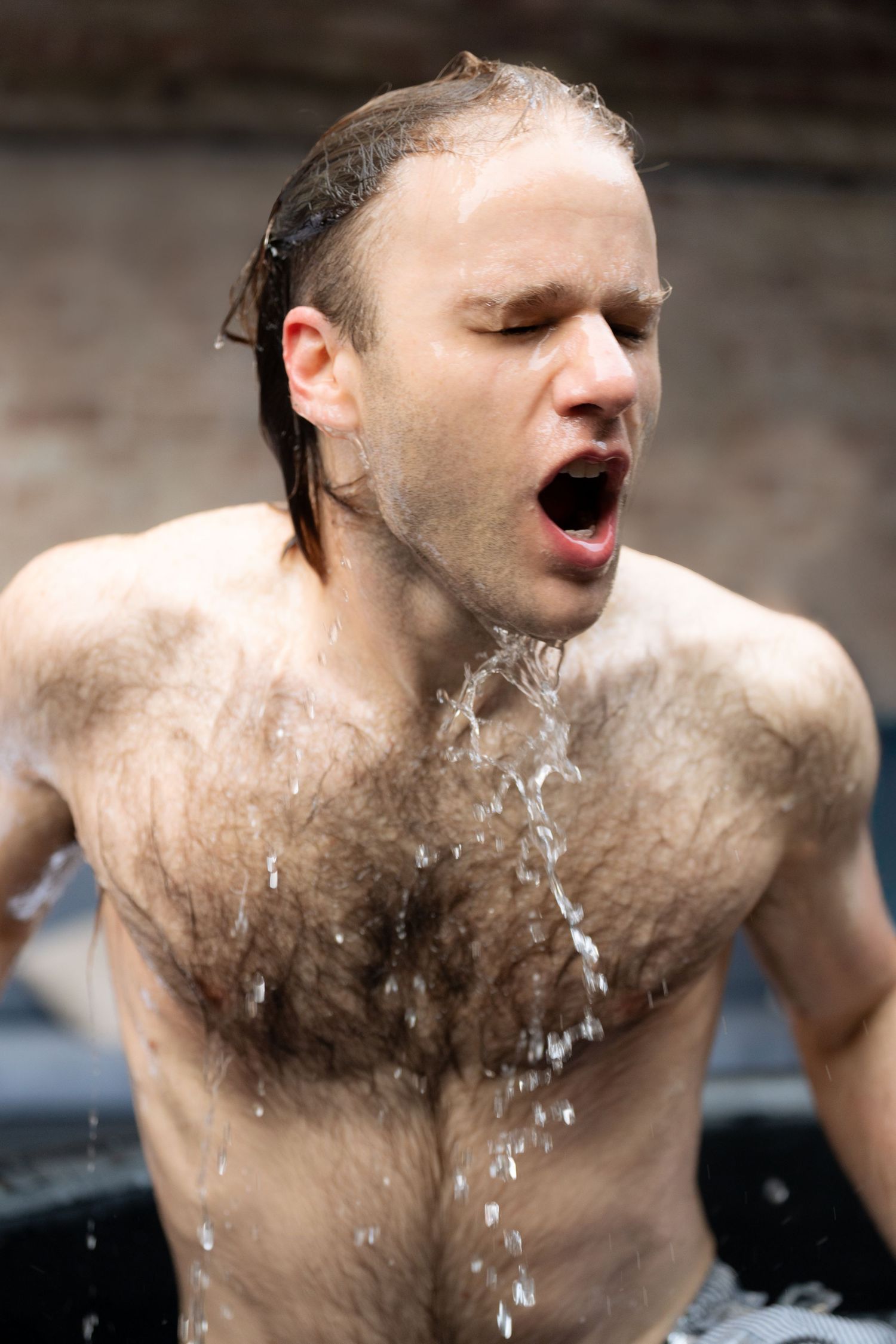 A person splashing water on themselves during an outdoor swim or bath with water droplets falling from their face and body.