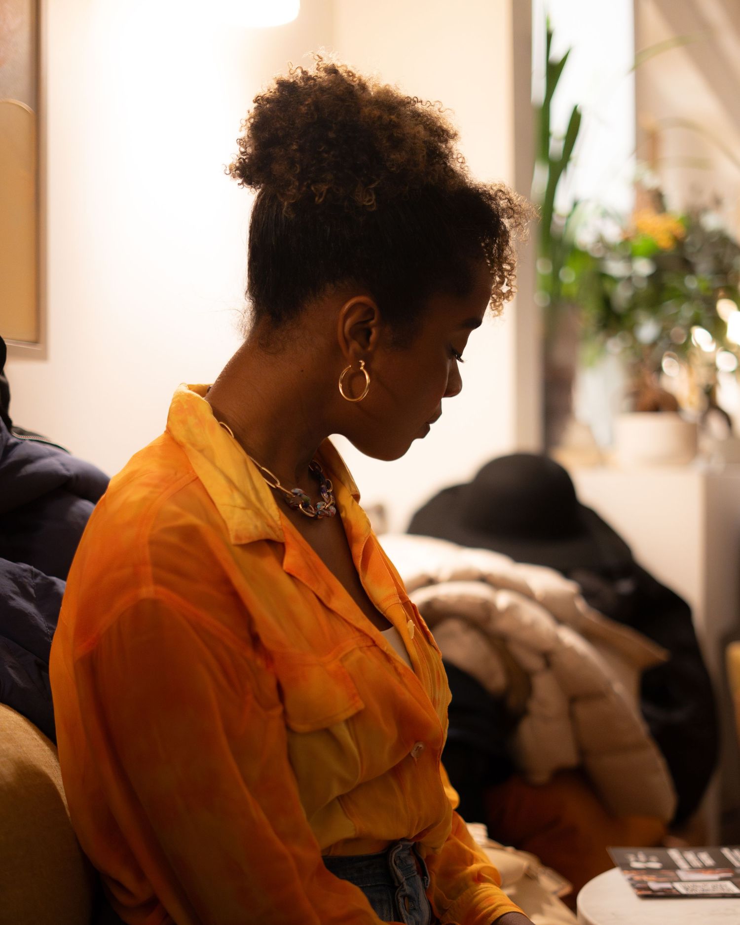 A candid side profile portrait of someone wearing a bright orange button-up shirt and gold hoop earrings.