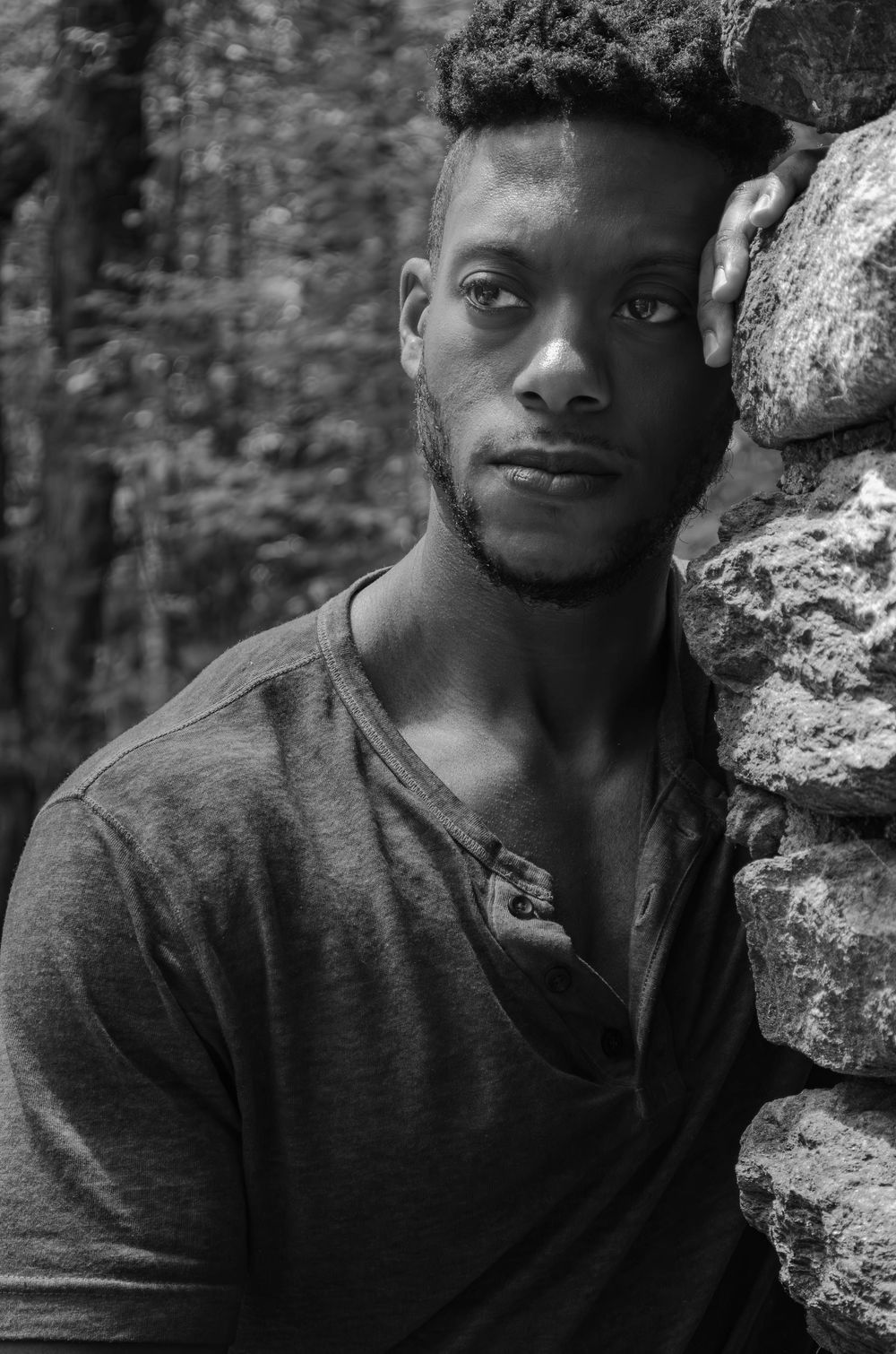 Black and white portrait series showing a person in a dark shirt leaning against a stone wall with varying expressions.