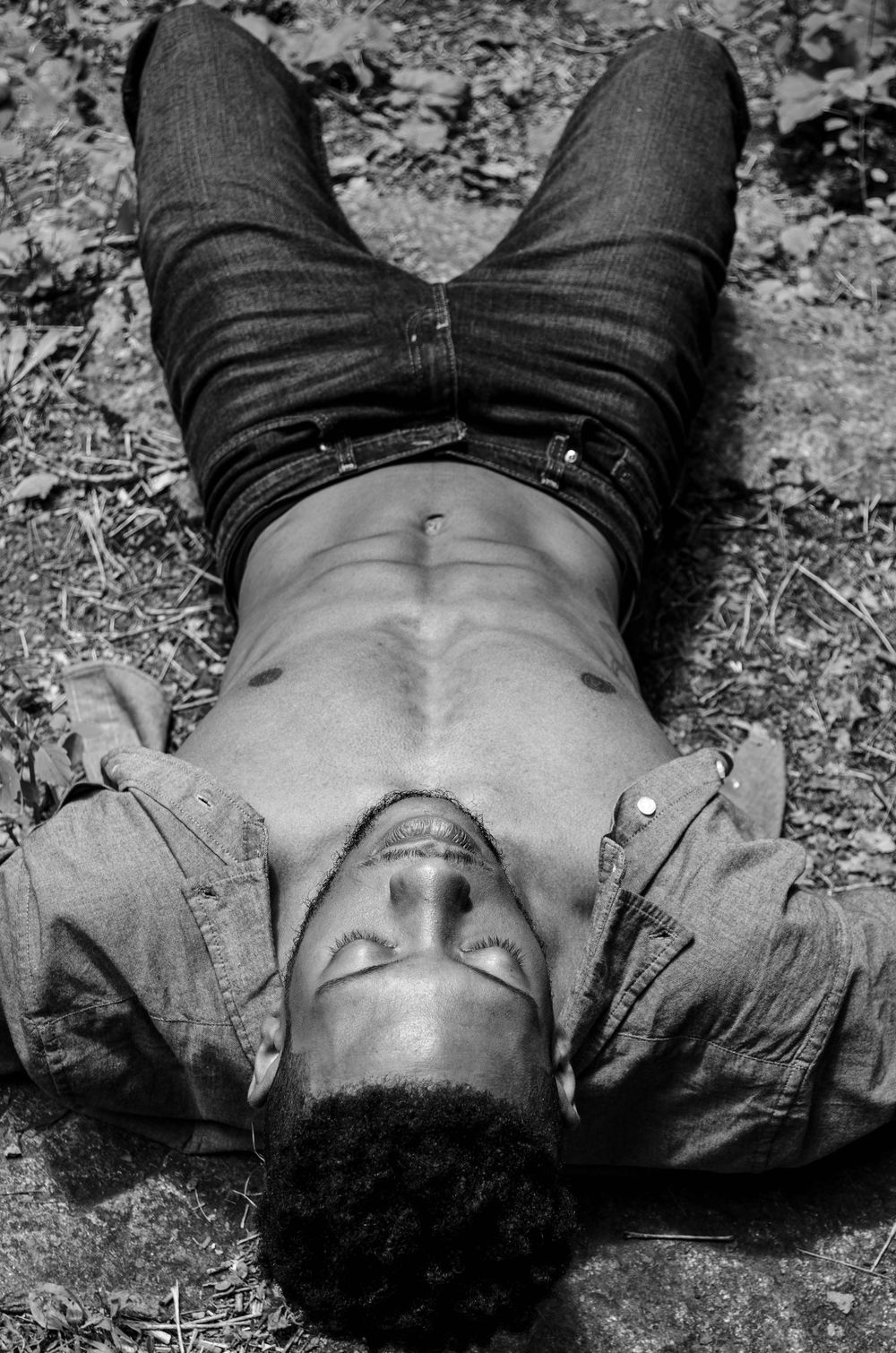 Black and white photograph showing a person lying on the ground in casual attire.