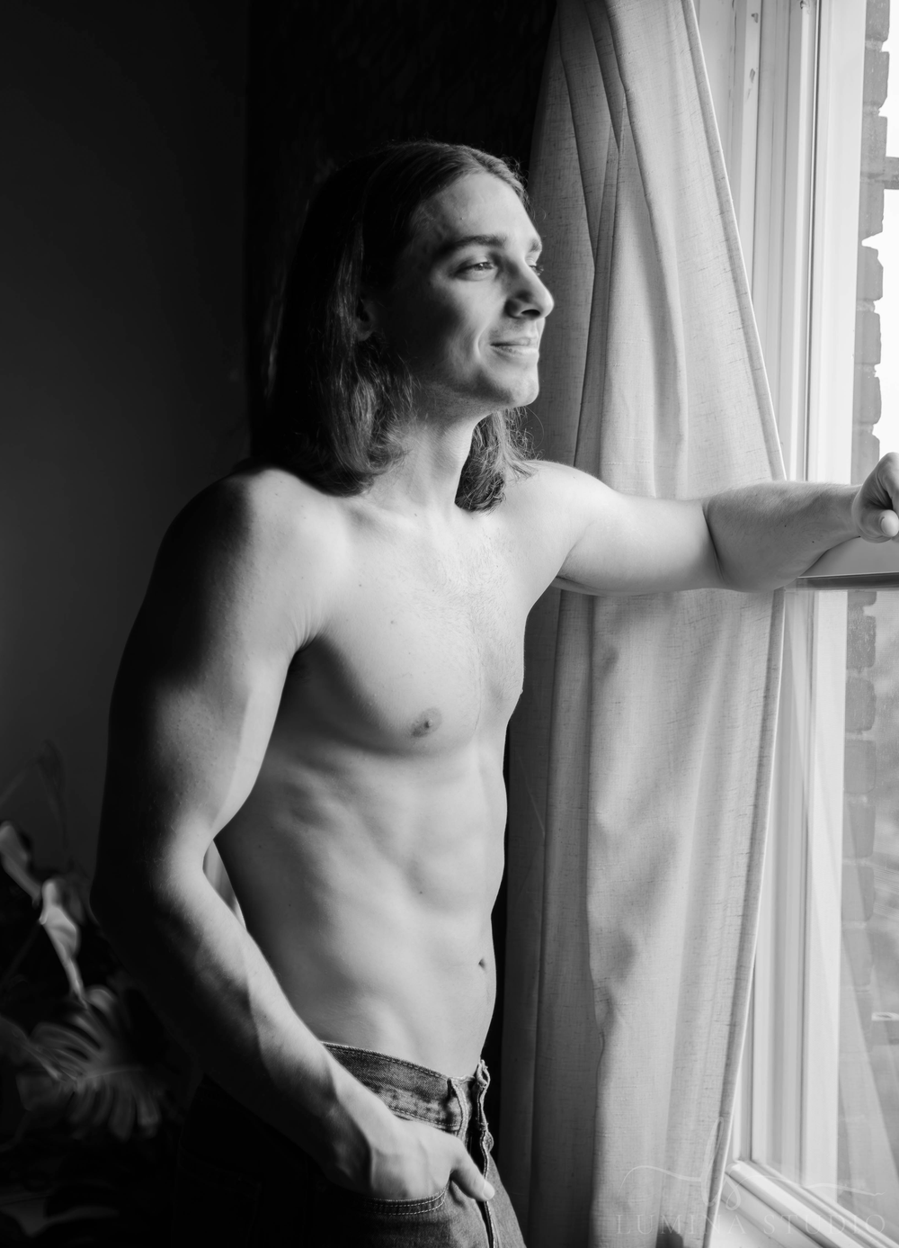 Men's Boudoir. Dudeoir. Black and white portrait of person standing by window with gentle lighting.