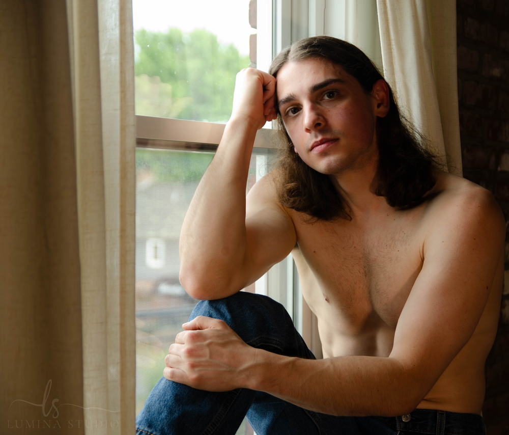 Men's Boudoir. Dudeoir. Pensive figure rests against window frame in natural lighting.