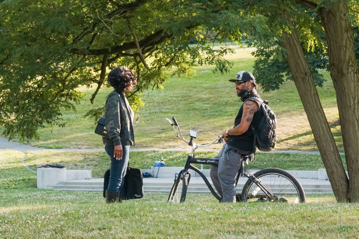 Two photographers with camera equipment and a bicycle enjoying a sunny day in a tranquil park setting.