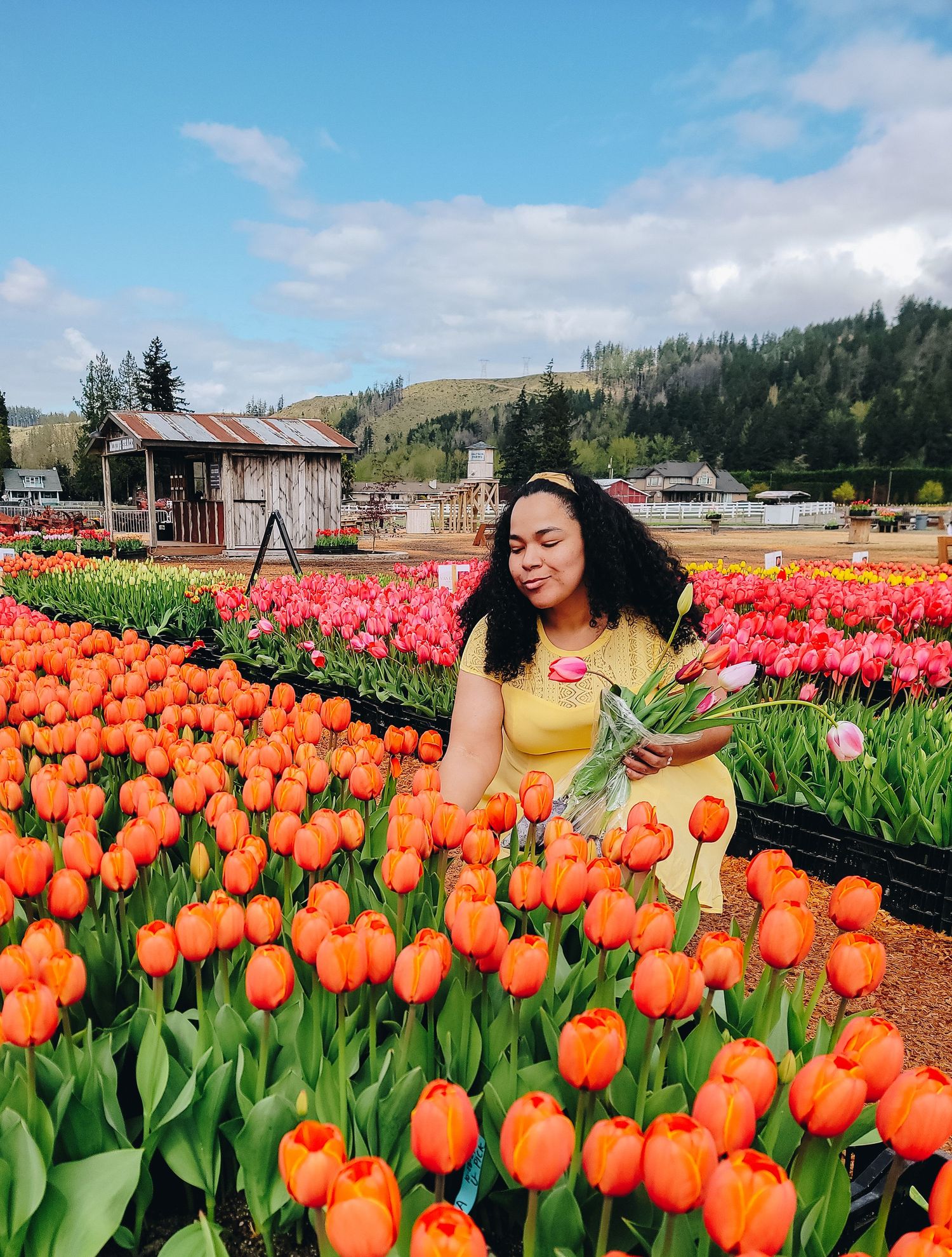 Photographer posing among orange tulips and scenic mountain views in Sumner, WA.
