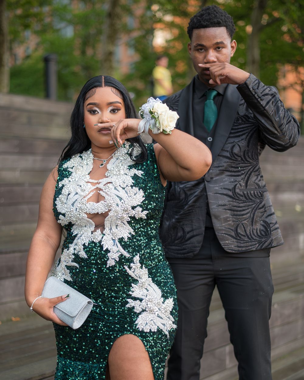 A couple poses on steps, with her in a sequined green dress and him in a black suit.