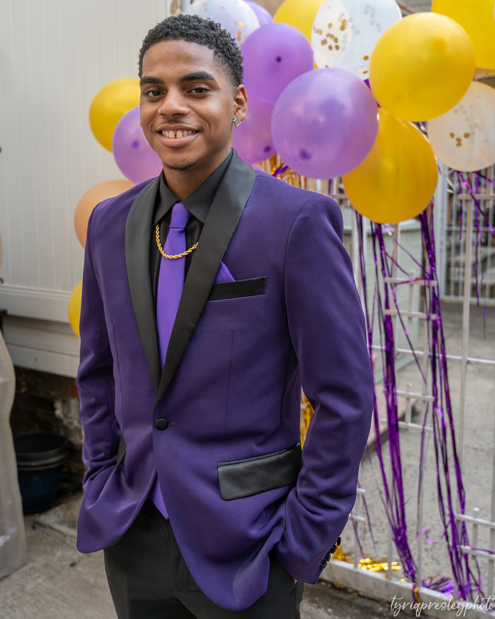 A person in a purple suit jacket smiles in front of colorful balloon decorations.