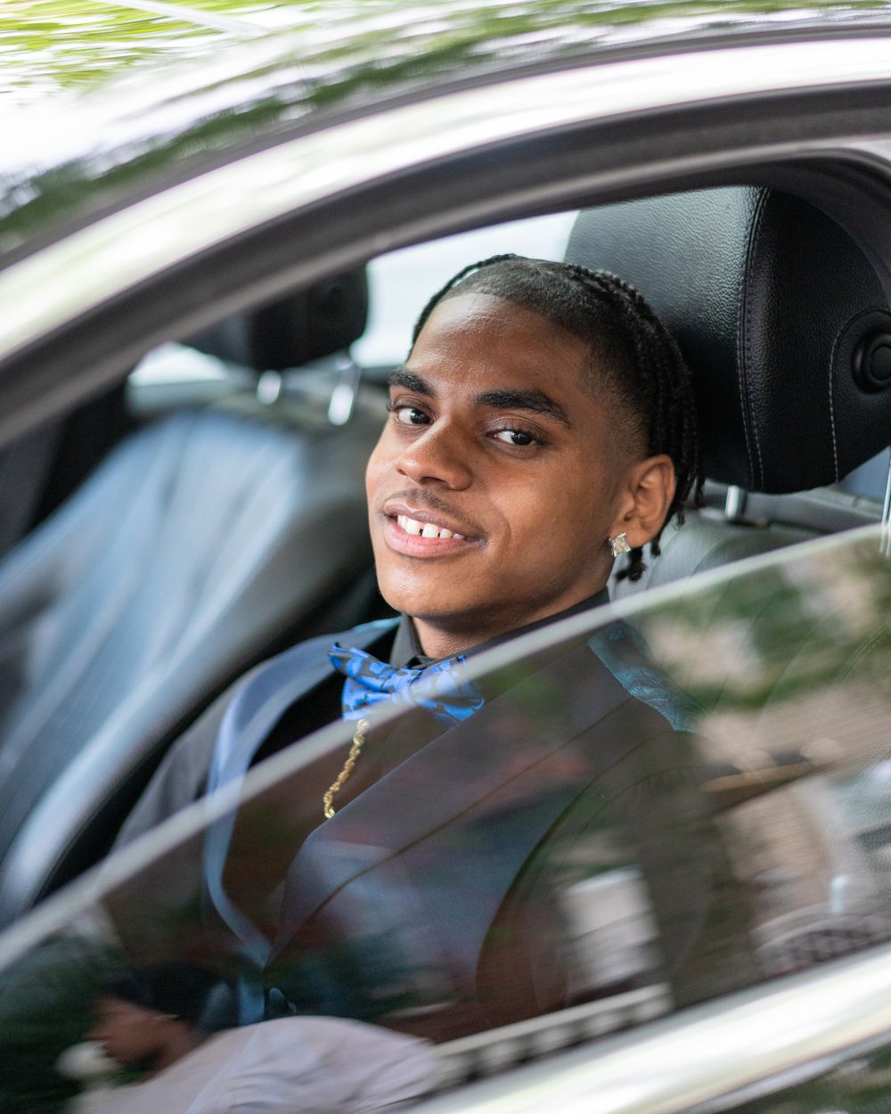 Young driver smiling while sitting behind the wheel of a car wearing a blue shirt and tie.