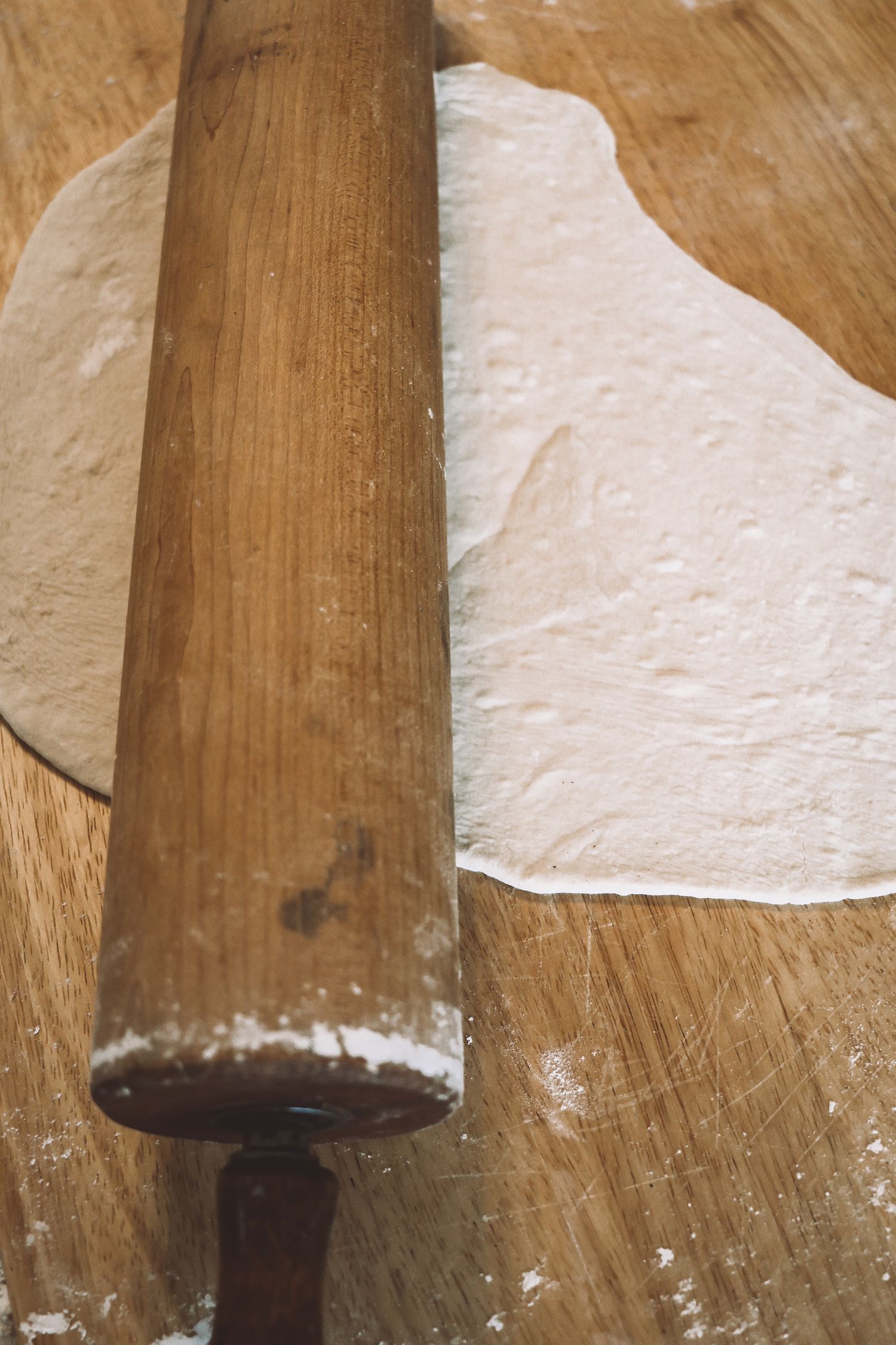 Wooden rolling pin rests on flour-dusted dough and wooden surface while baking.