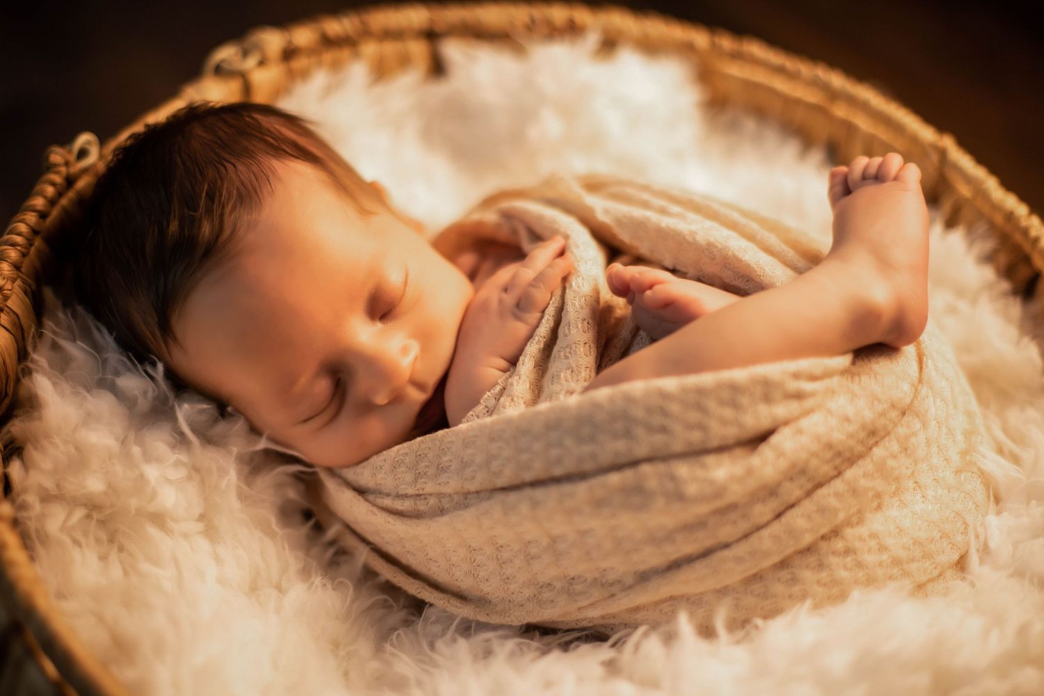 Newborn baby swaddled and curled up on a white fur blanket