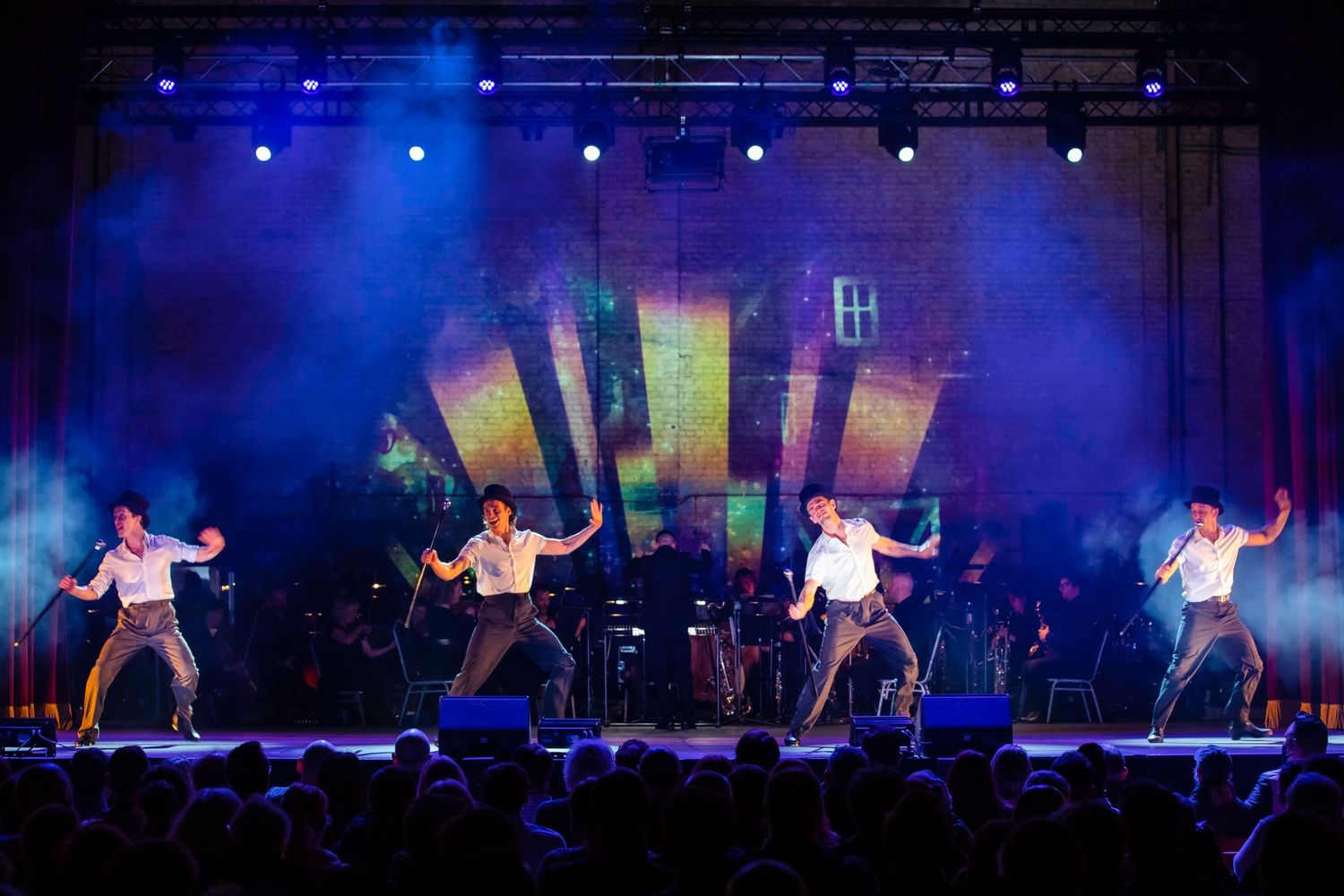 Energetic dance performance with synchronized dancers under blue lighting on concert stage.