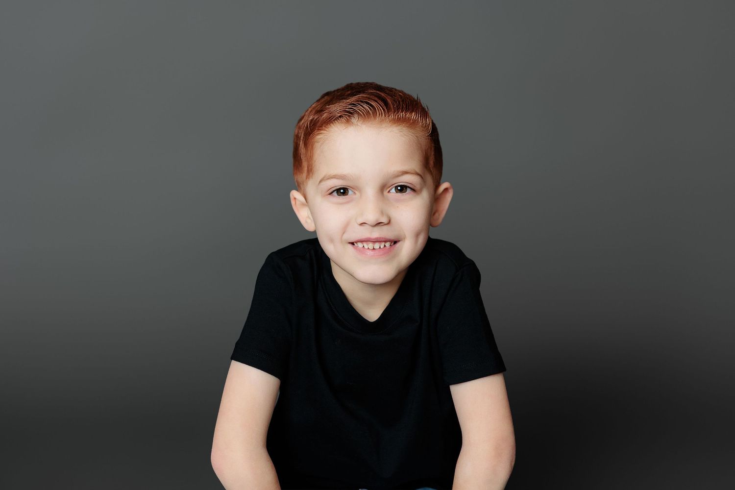 A young child in a black t-shirt poses for a series of connected portrait photos against a dark background.