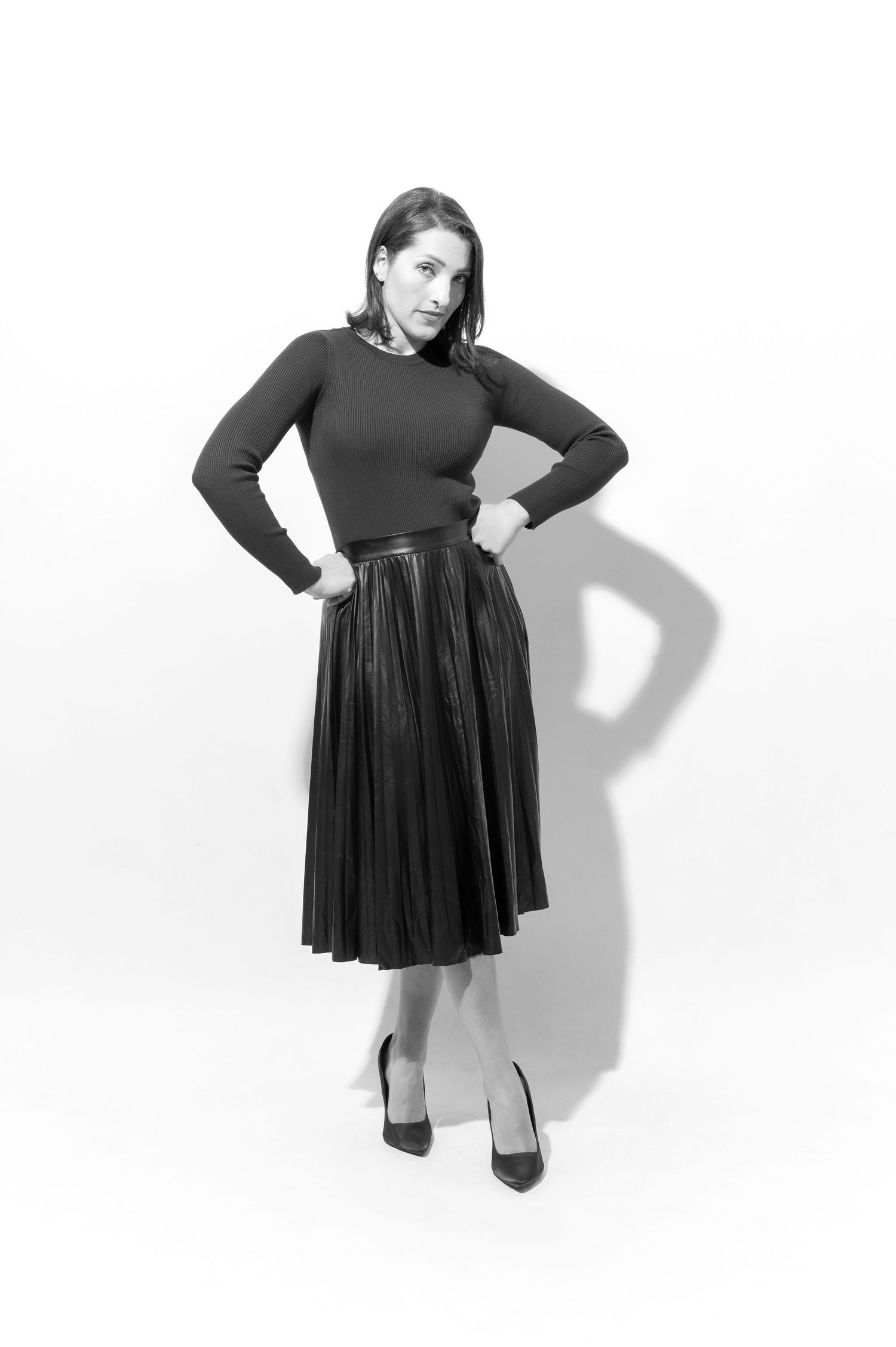 Four fashion poses showing a black long-sleeve dress with pleated skirt and heels against a white backdrop.