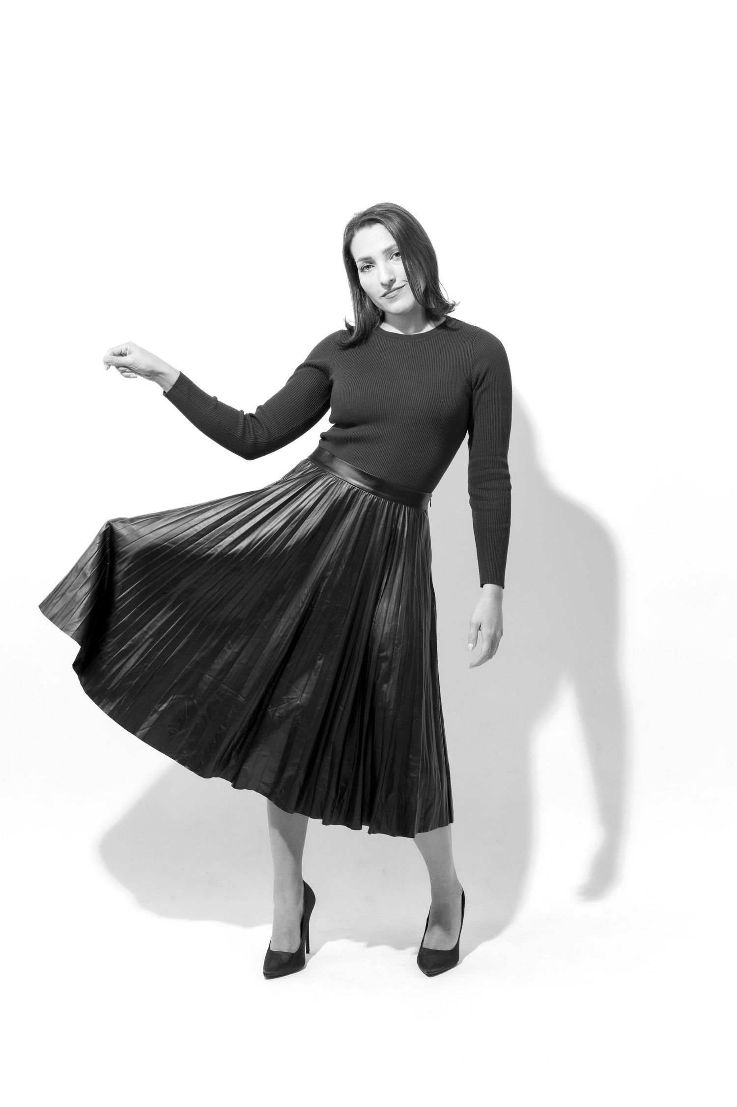 A figure in a black long-sleeved dress performs a flowing dance movement sequence against a white background.