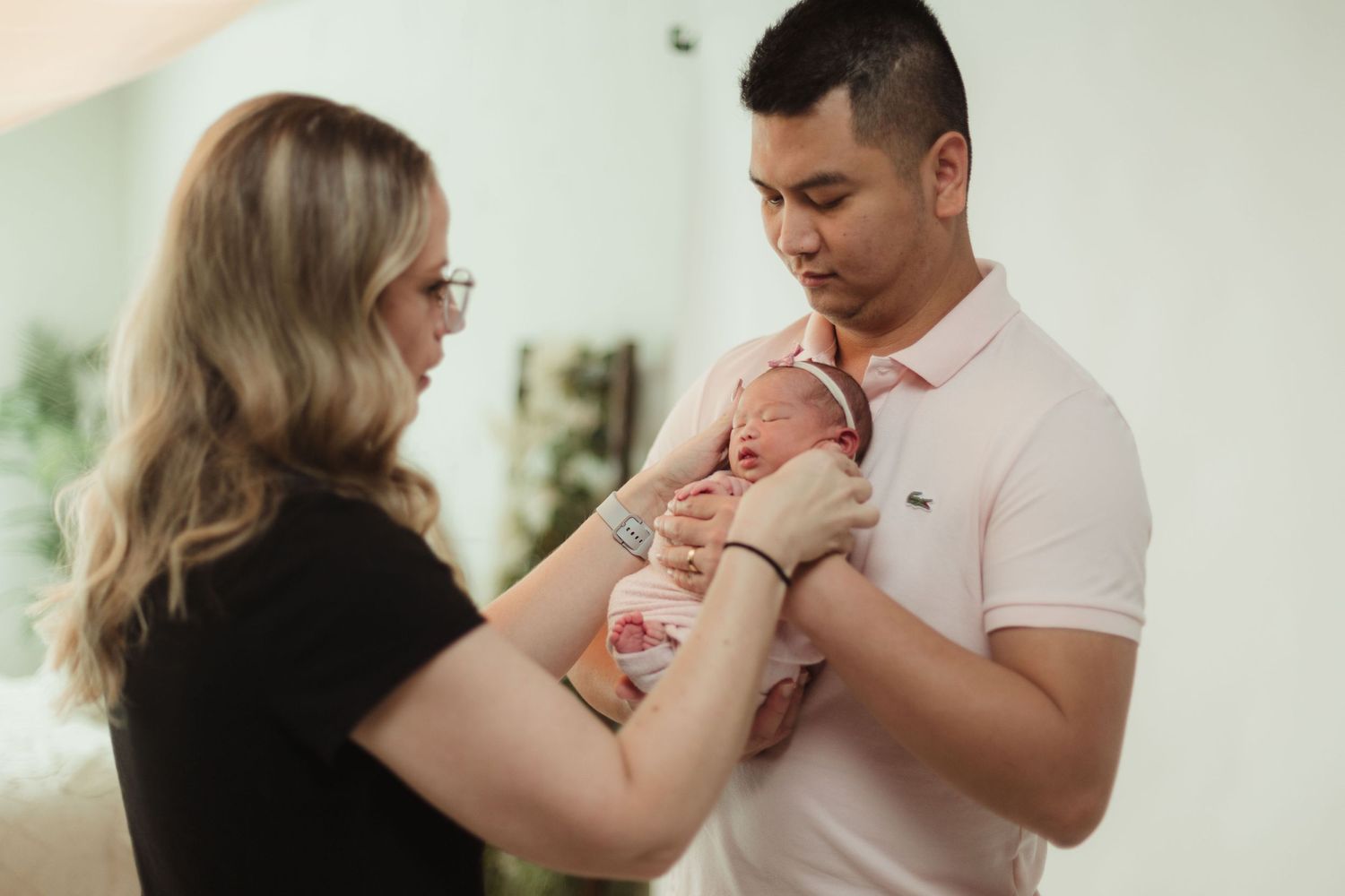 Intimate newborn photography session showing gentle interaction with baby in bright room.