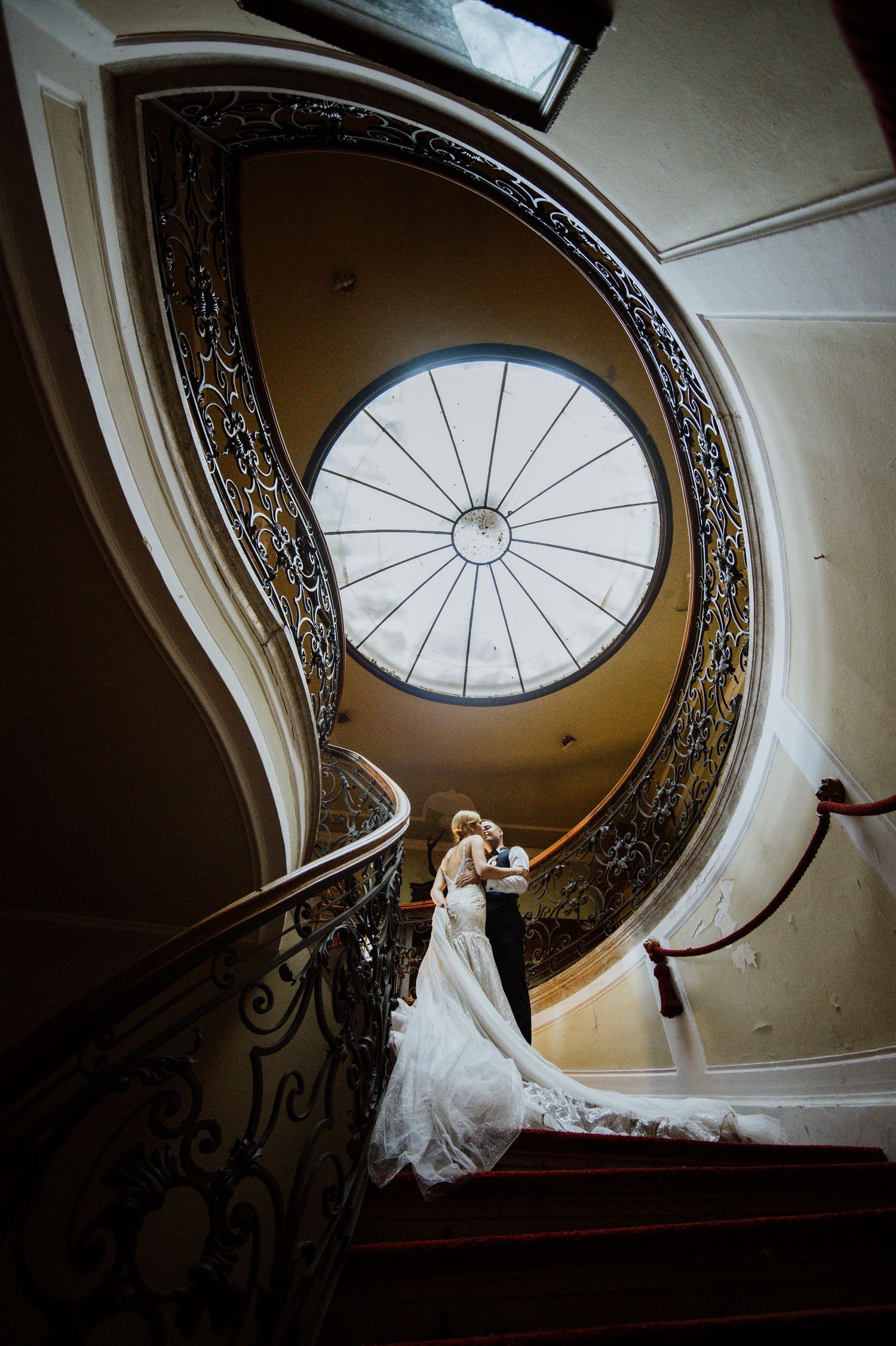 Dramatic wedding photograph on curved staircase beneath ornate circular skylight.