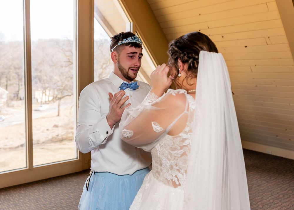 Emotional bride wiping tears as groom smiles during wedding first look in a rustic chapel venue.