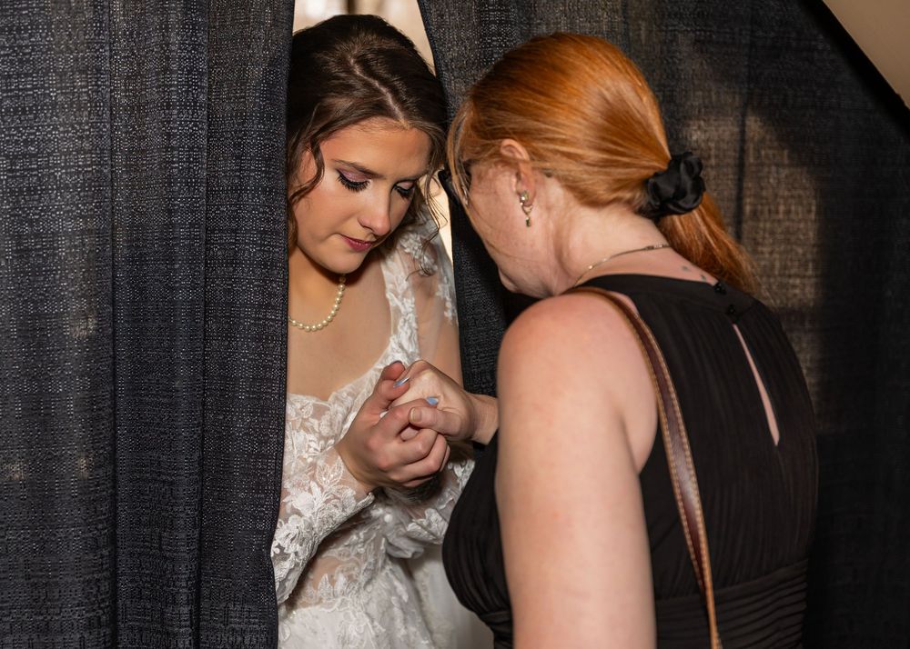Bridesmaid helping bride with wedding dress details before the ceremony in a candid moment.