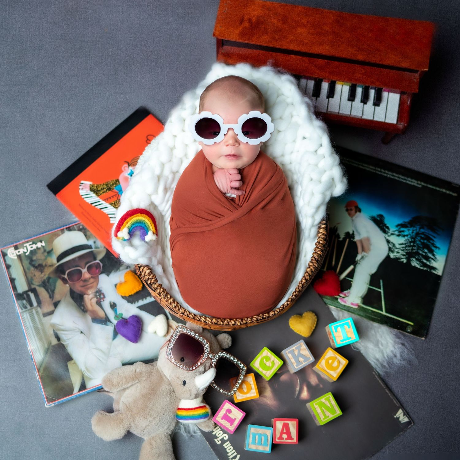 Creative baby portrait with toys, blocks, and musical instruments on gray background.