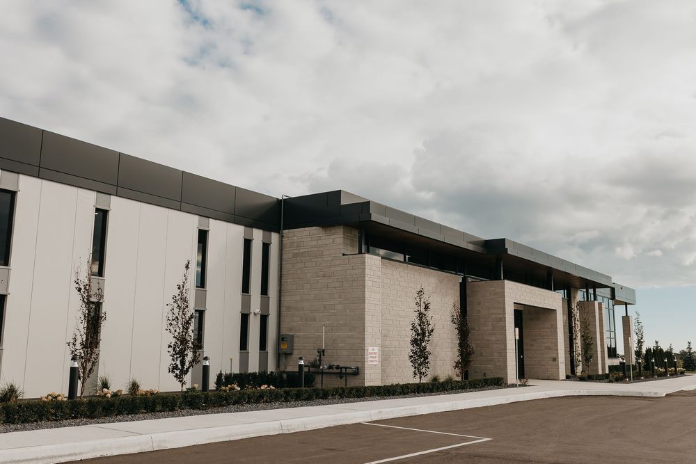 Modern commercial building with white and brick facade, large parking lot, and young trees under cloudy sky.