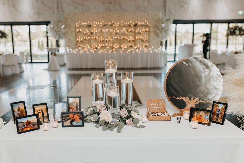 Elegant wedding reception table with framed photos, white floral arrangements, glass candle holders, and a decorative mirror display.