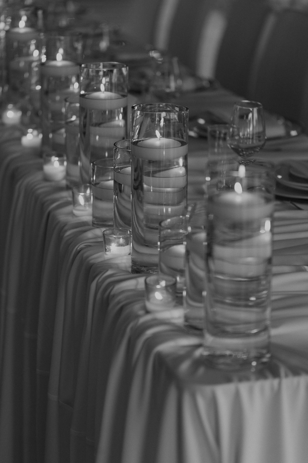 Elegant black and white photo of floating candles in glass cylinders on a draped banquet table.