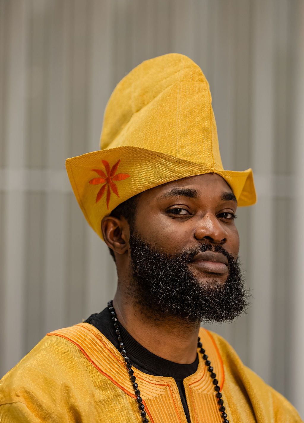 Portrait of bearded Black man wearing yellow traditional African fila hat with red star embroidery and beaded necklace.