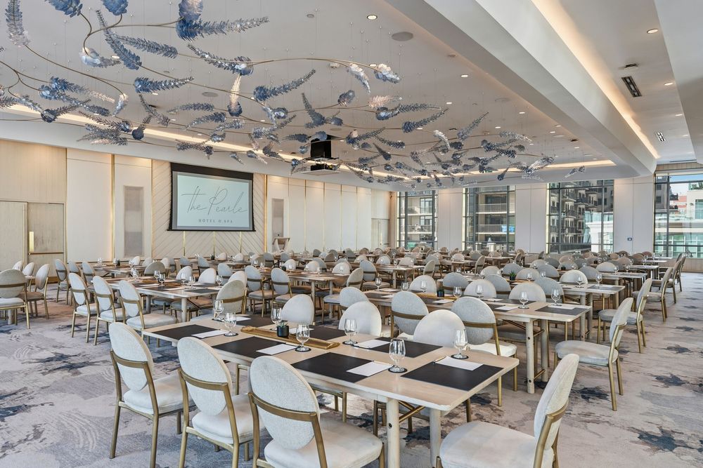 Modern cafeteria interior with white tables and chairs arranged in rows under decorative hanging light fixtures.