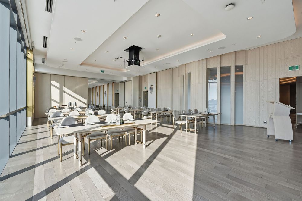 Modern office space with light wood floors and floor-to-ceiling windows offering panoramic city views and natural lighting.