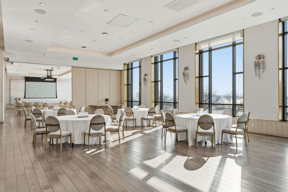 Elegant dining space featuring white tables and chairs arranged in rows with natural light streaming through windows.