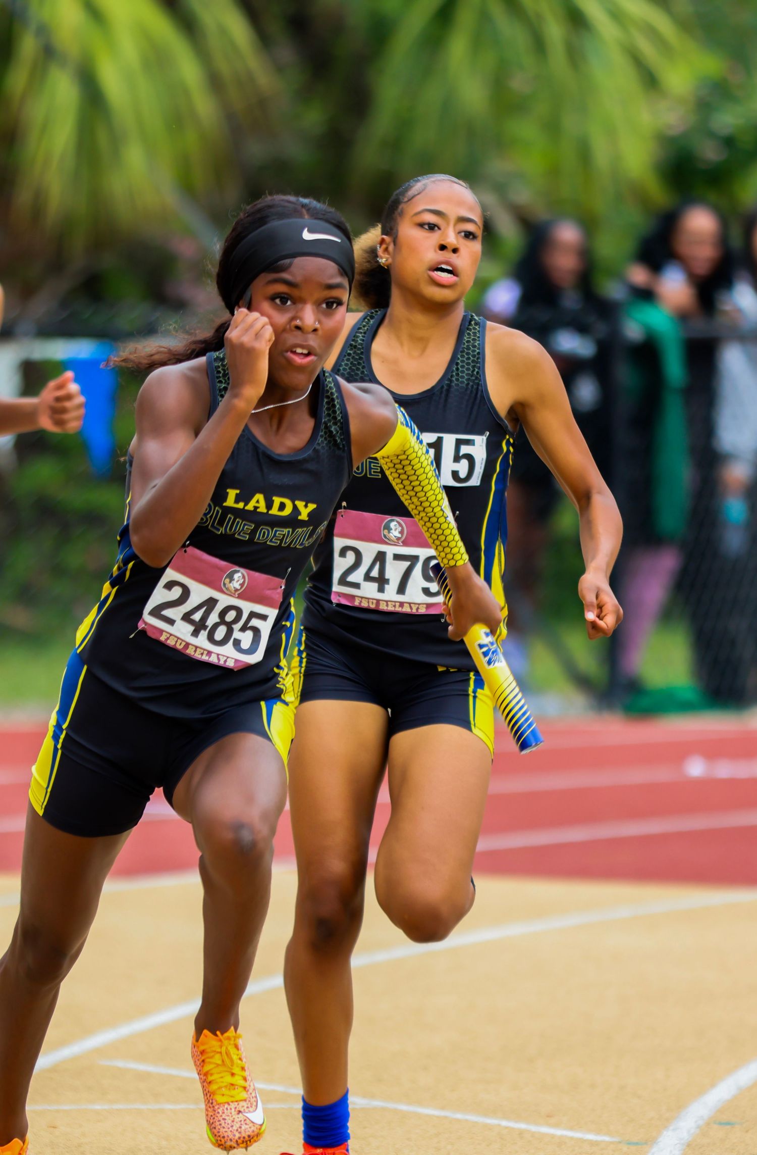 Track athletes compete in sprinting event on outdoor track during daytime competition.