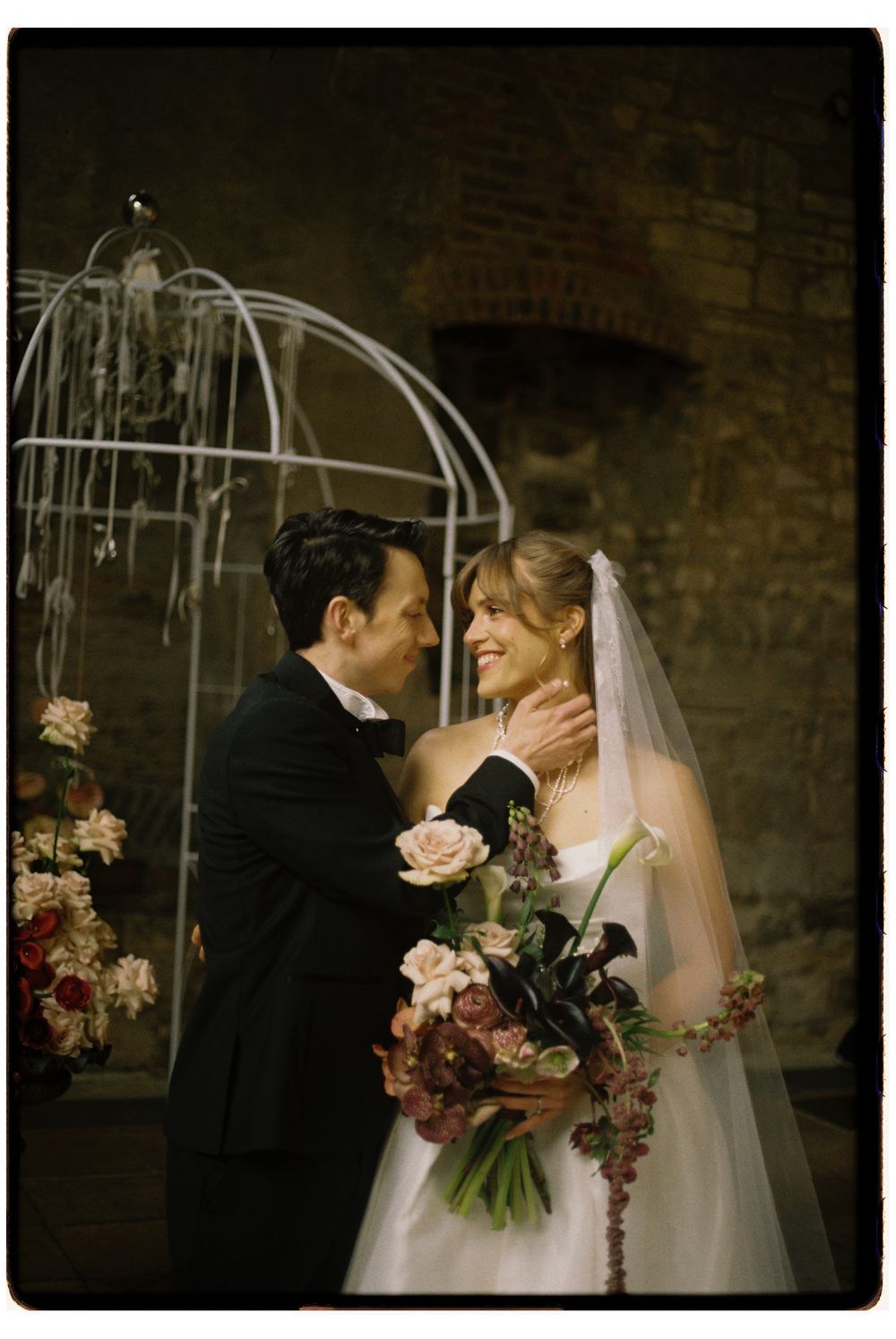 A romantic wedding moment captured in moody lighting against exposed brick walls with soft pink floral arrangements.