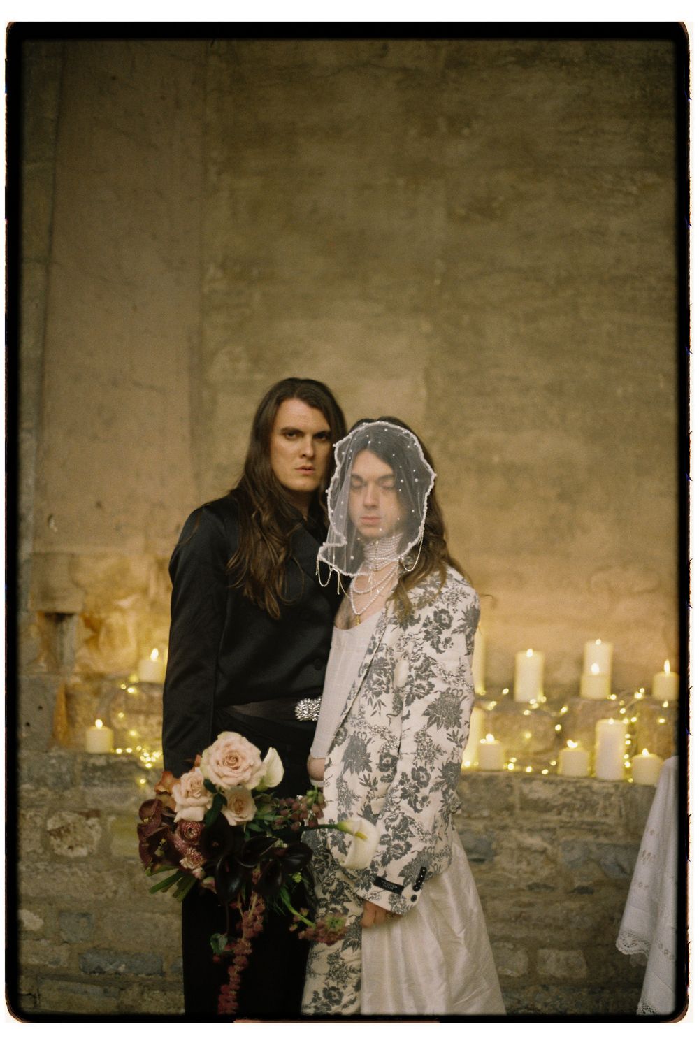 A romantic candlelit scene with a couple in formal wear against a stone wall backdrop.