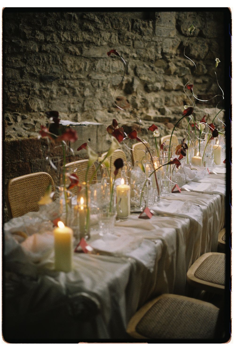 Elegant table settings with white linens, glowing candles, and red floral accents create a romantic dining atmosphere.