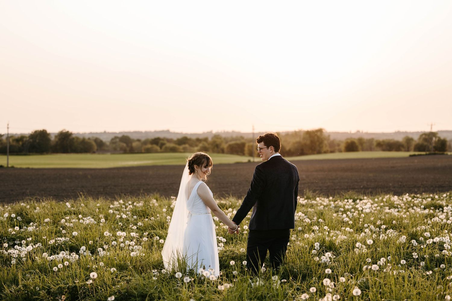 A wedding couple stands in a meadow of wildflowers at sunset.