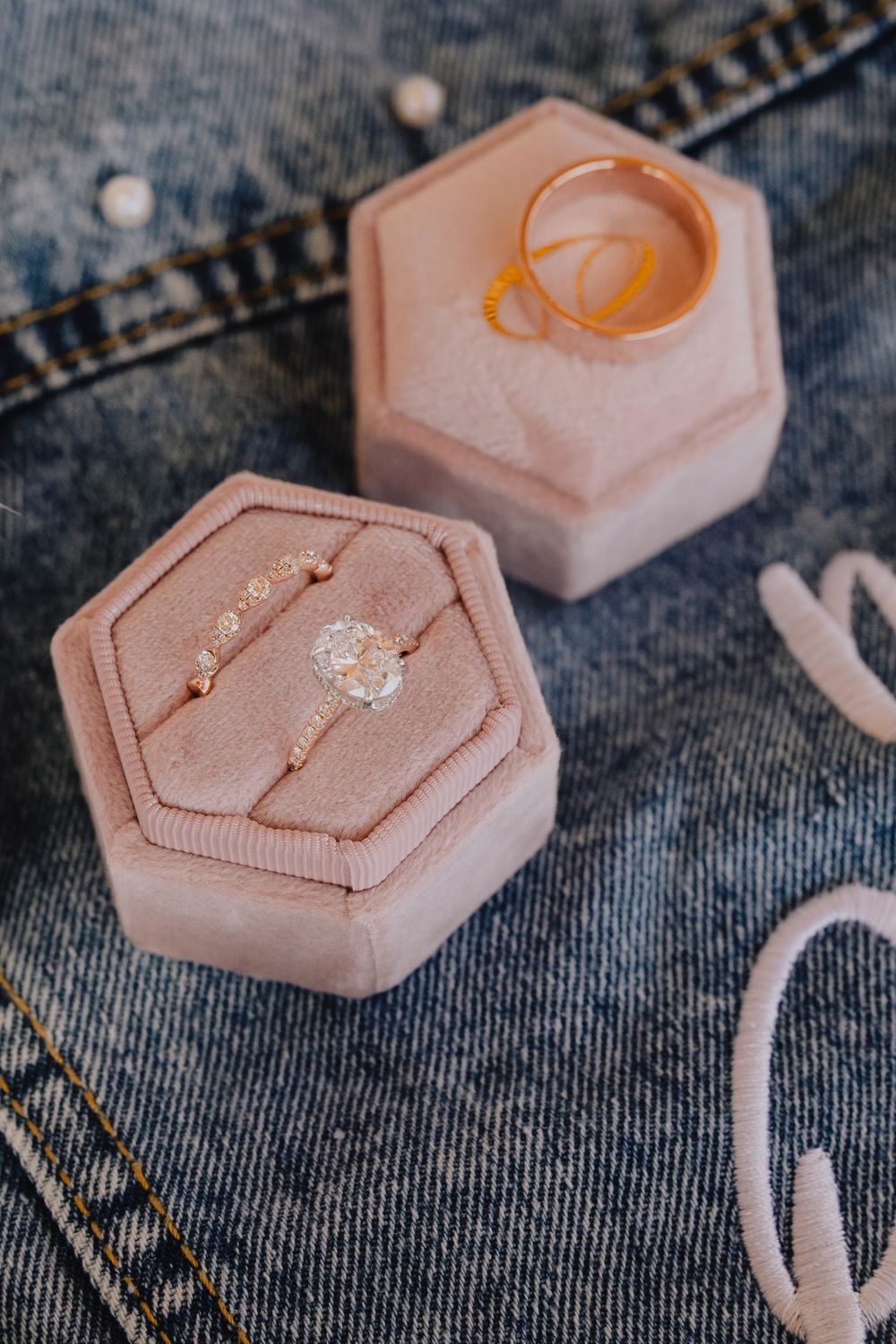 Diamond engagement ring and gold wedding bands displayed in pink velvet hexagon ring box on denim.