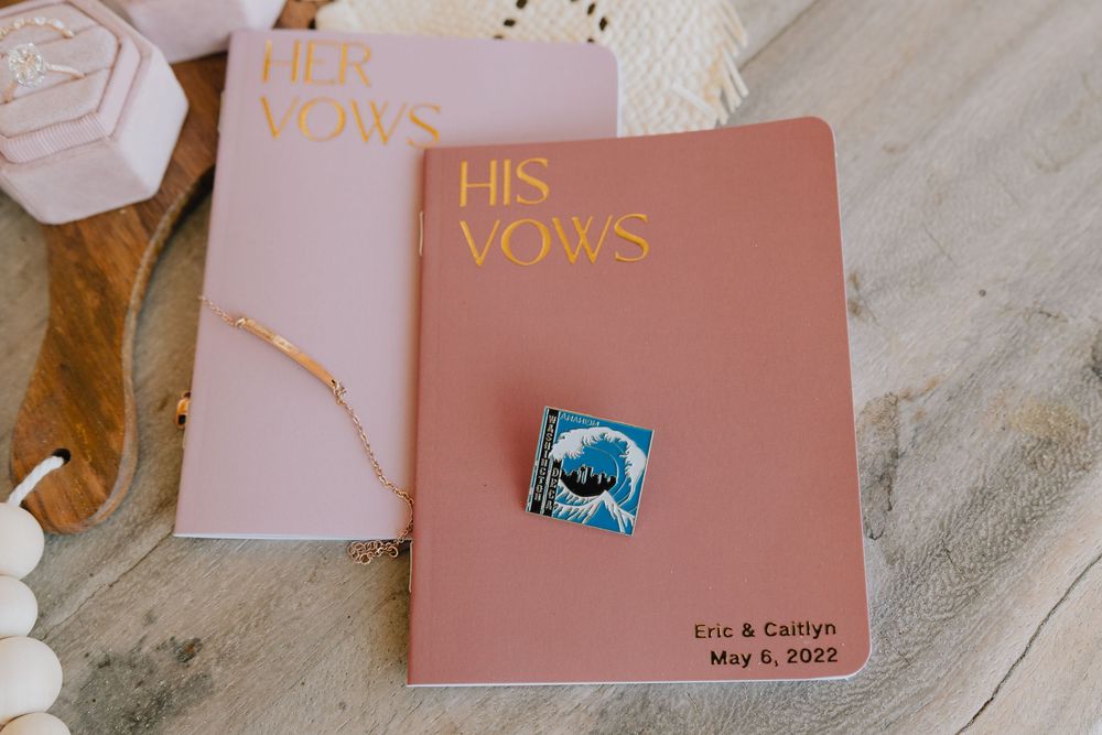 His and Her Vows books with a decorative pin on a neutral background for a wedding ceremony.