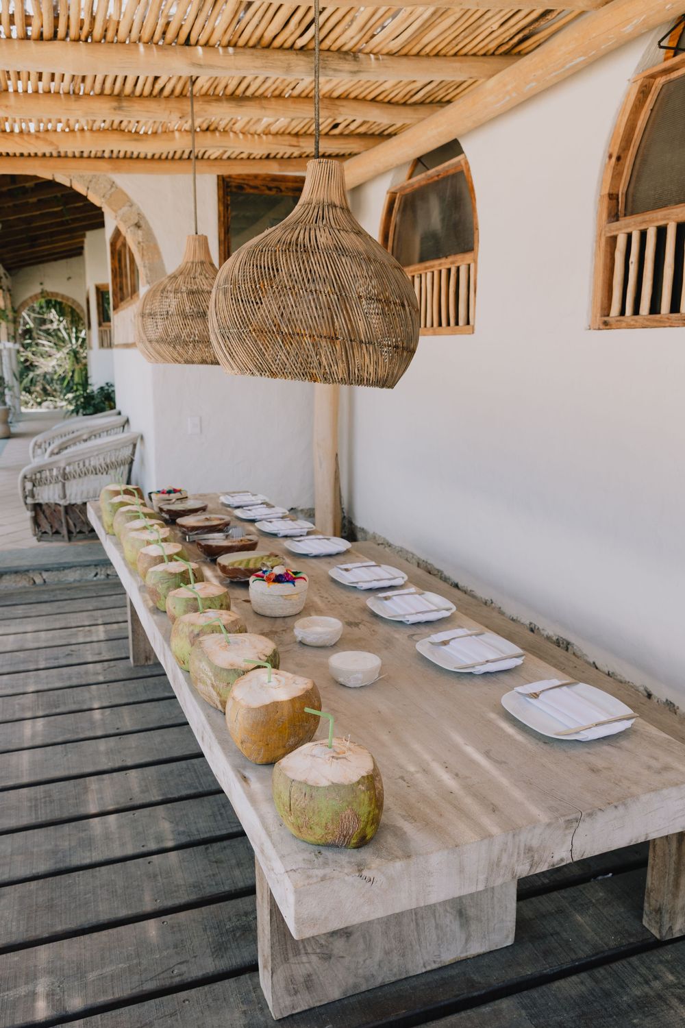 Rustic outdoor dining table set with fresh coconuts and wicker pendant lights at a tropical beach resort.