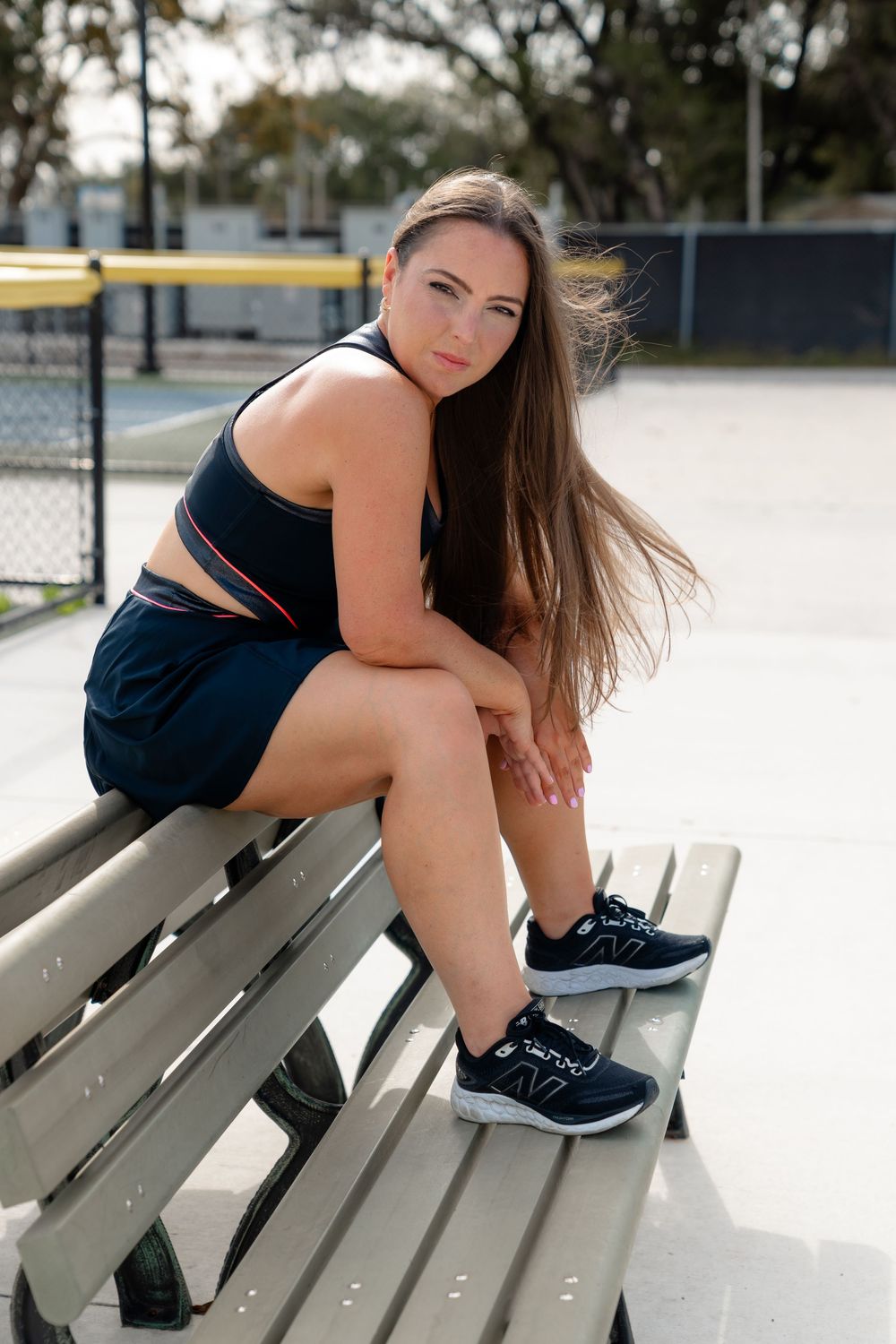 Athletic woman in navy sportswear sits on wooden bench at tennis court.