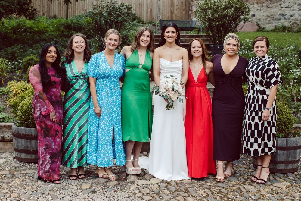 Group of people wearing colorful dresses pose together outdoors in a garden setting.