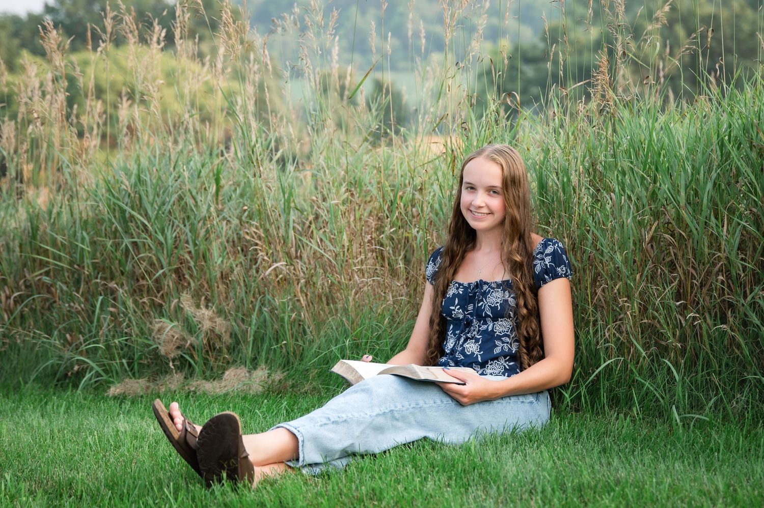 A person in a blue floral dress poses for outdoor portraits in tall grass during golden hour.