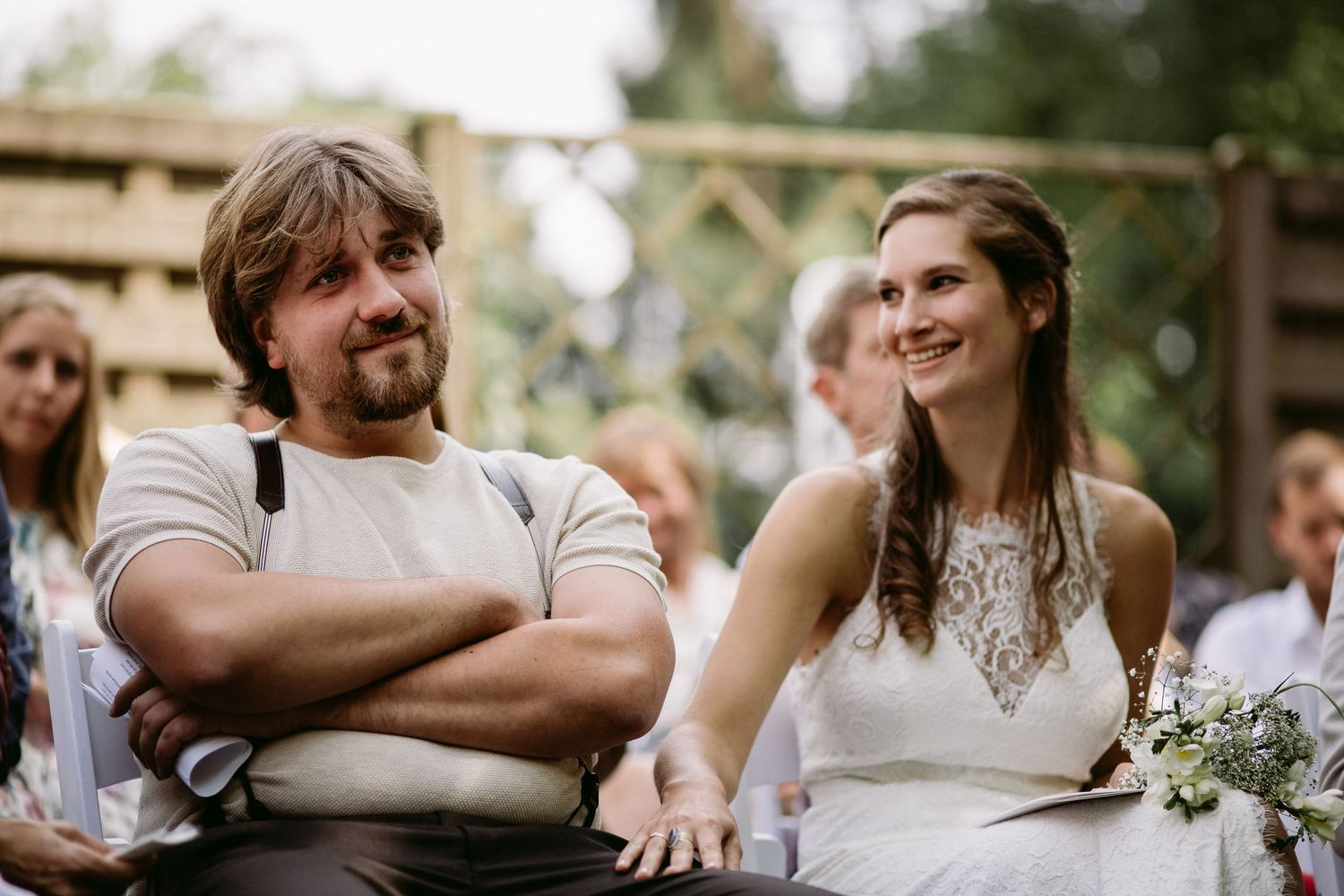 Casual outdoor wedding scene with couple sitting at rustic wooden table.