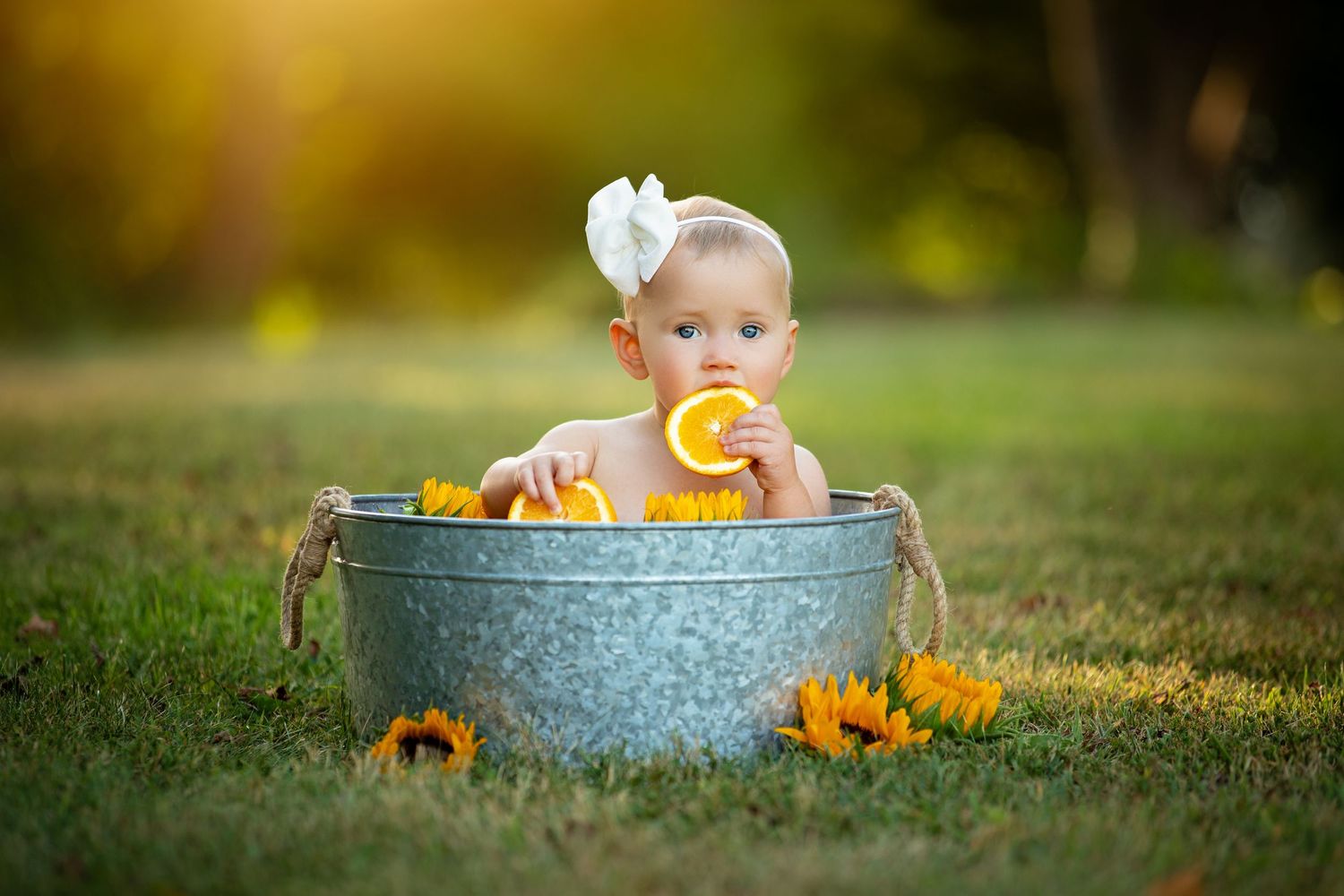 Baby in a blue metal tub surrounded by fall pumpkins and autumn foliage in an outdoor setting.